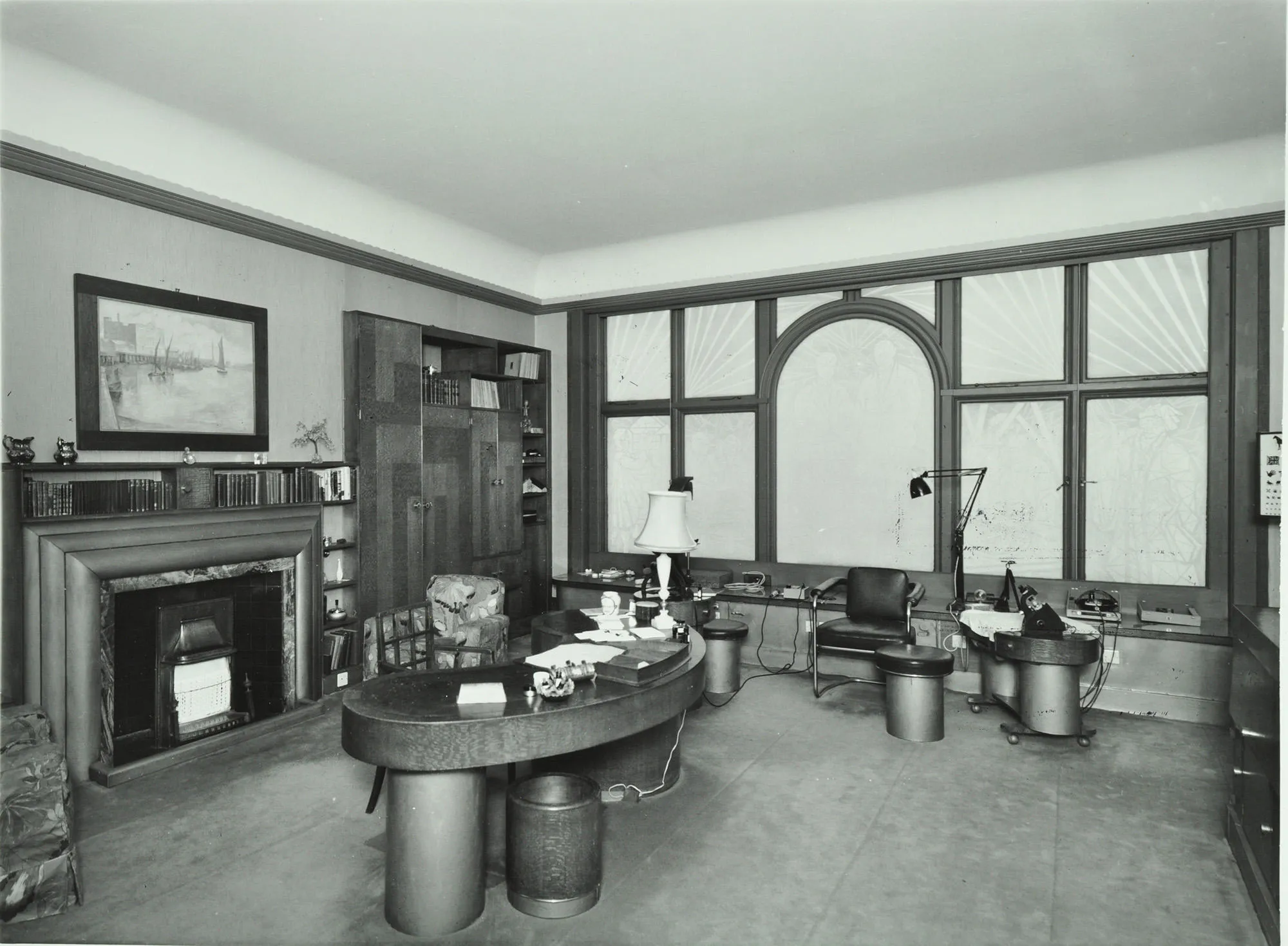 A room with a curved desk and stools by a fireplace