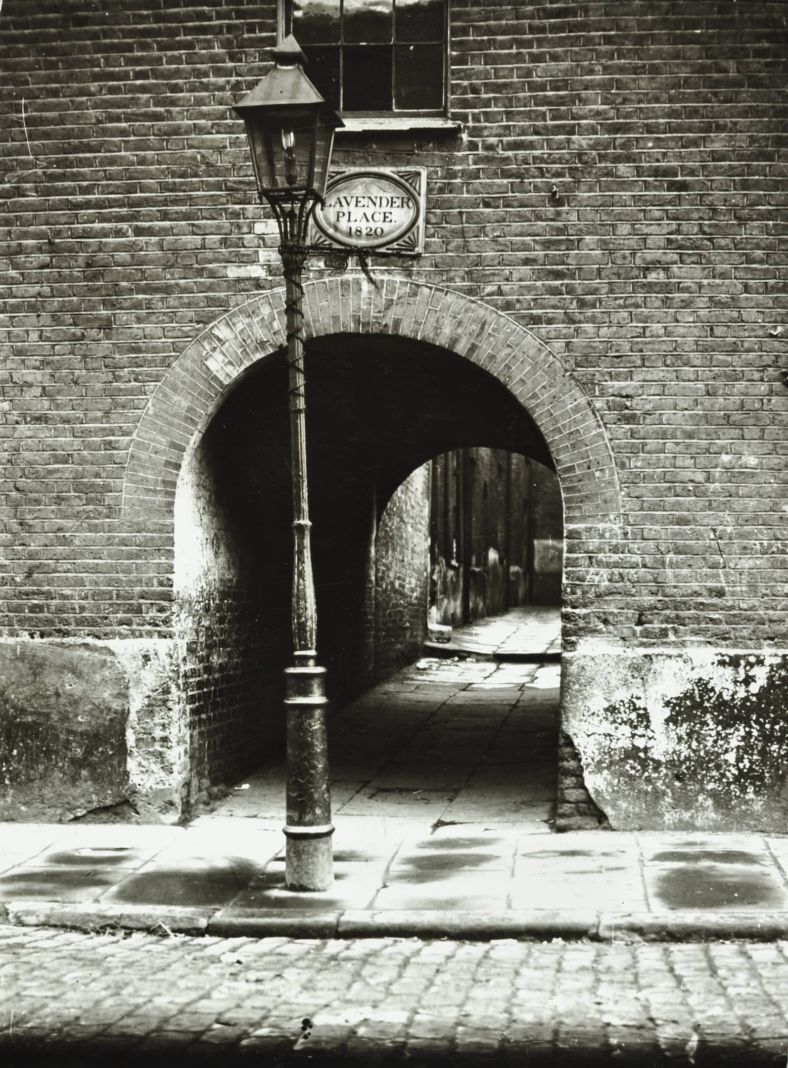 an archway in a wall with cobbled paving and an old gas lamp in the foreground