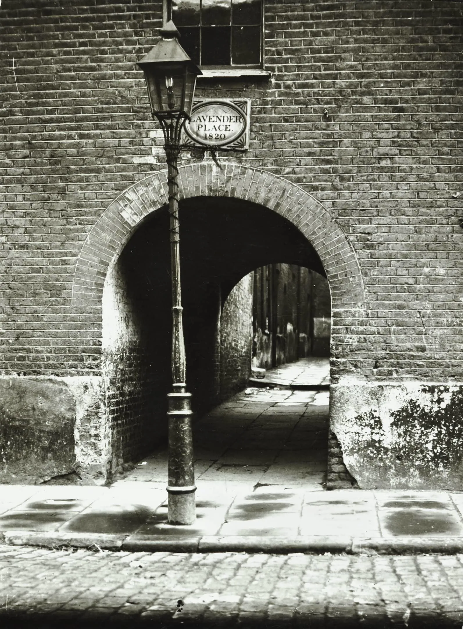 an archway in a wall with cobbled paving and an old gas lamp in the foreground