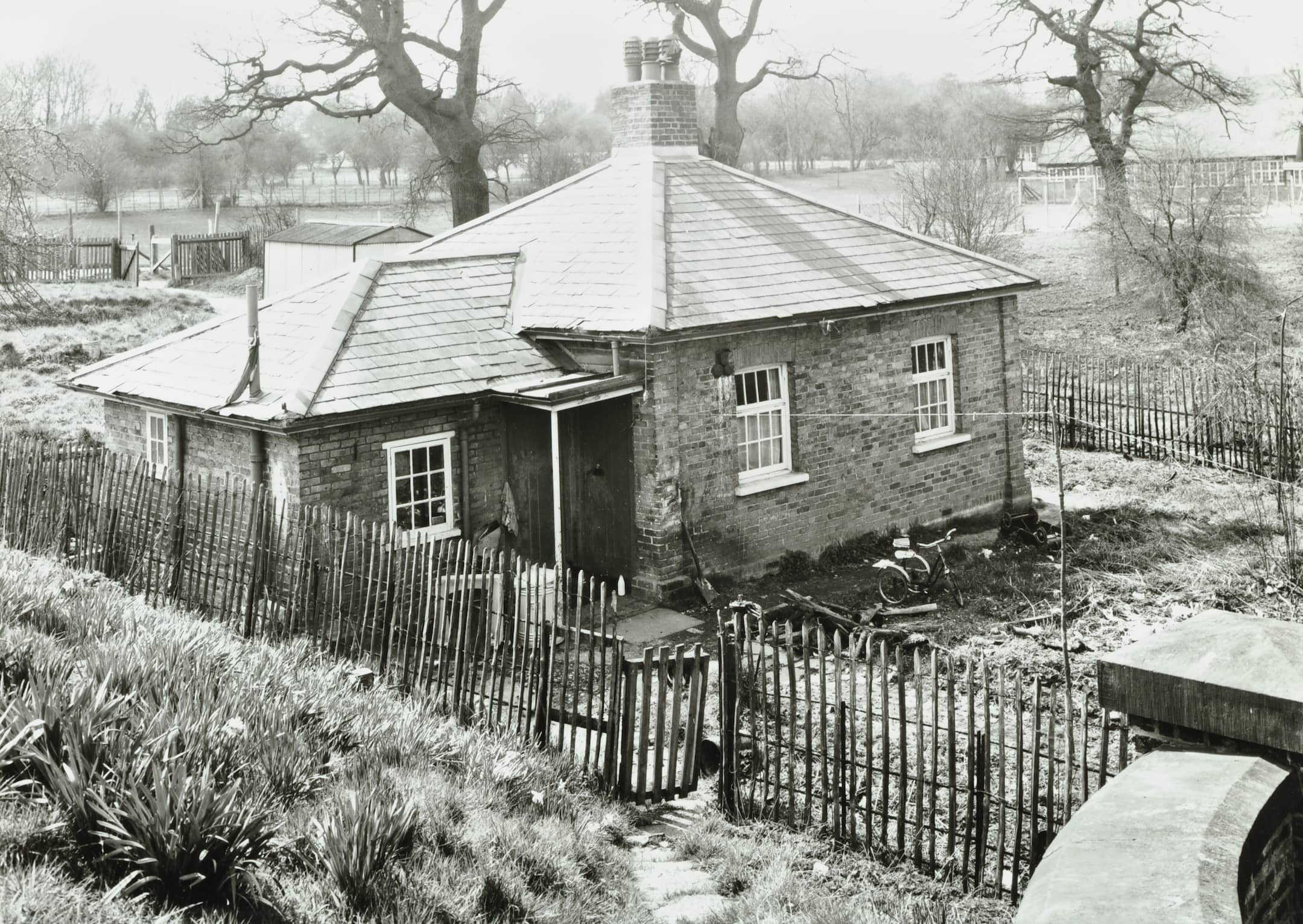 a small one storey building with a river in the background and a fence and grassy bank in the foreground.