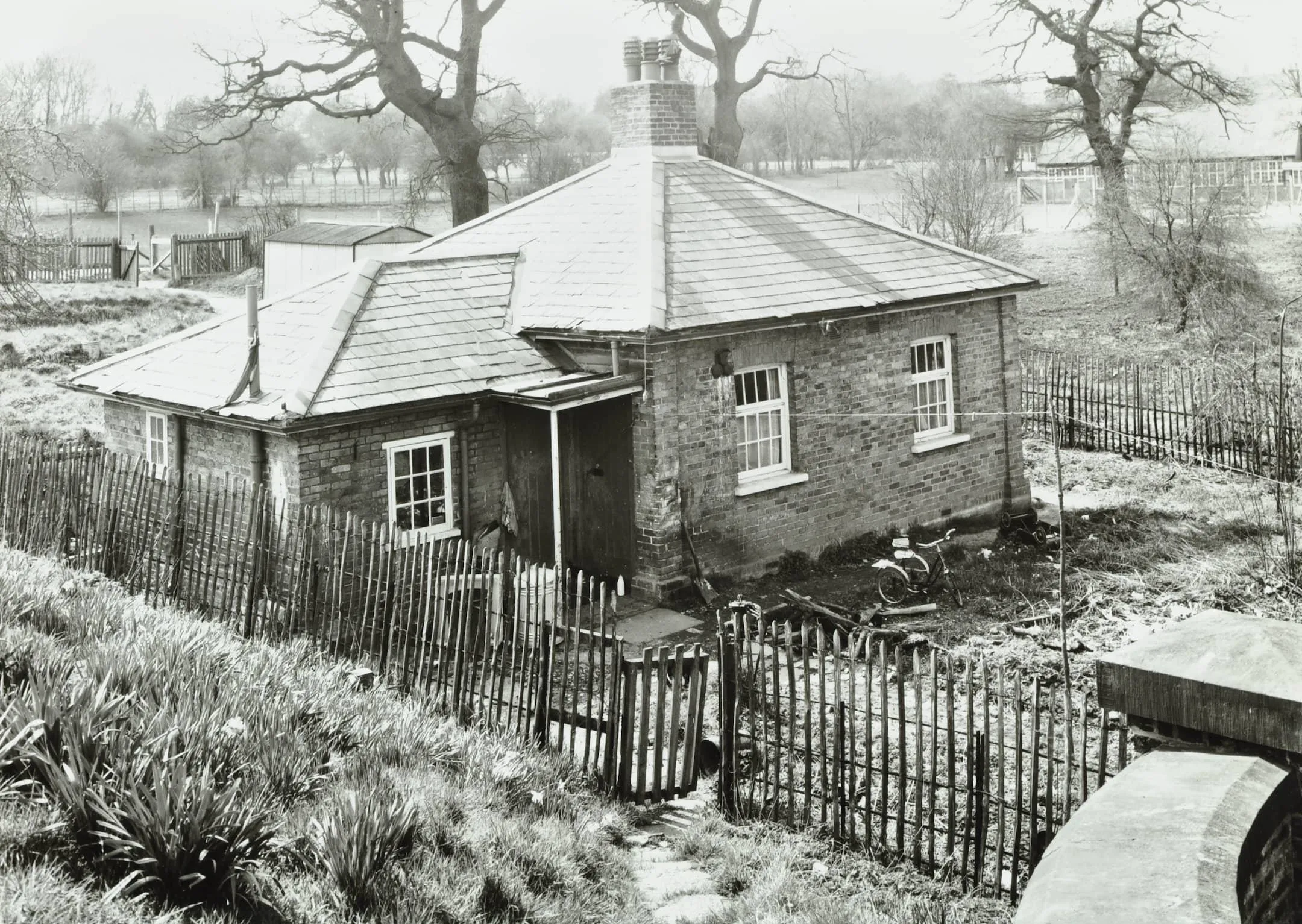 a small one storey building with a river in the background and a fence and grassy bank in the foreground.