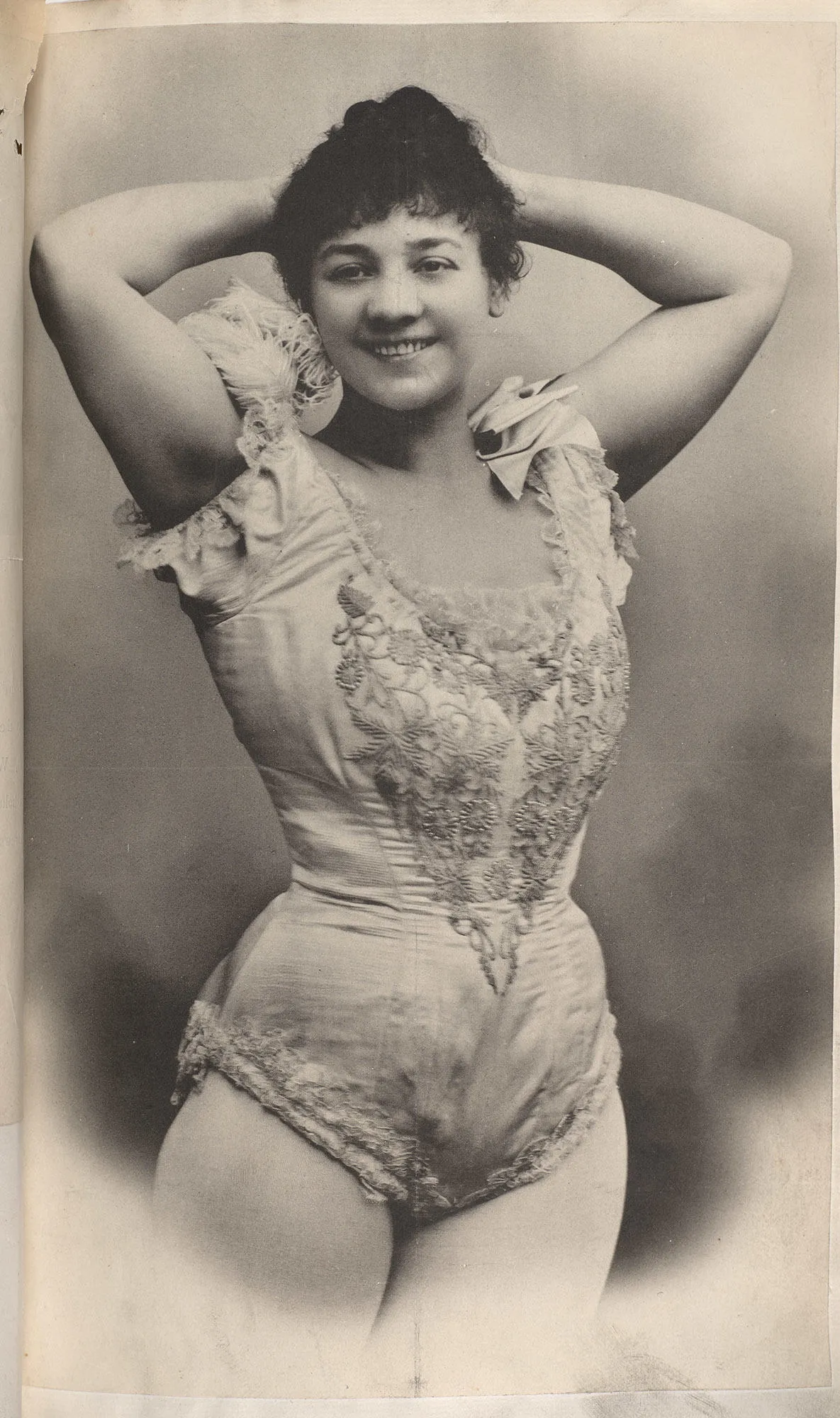 photograph of a woman with arms up behind her head and in a gymnasts outfit