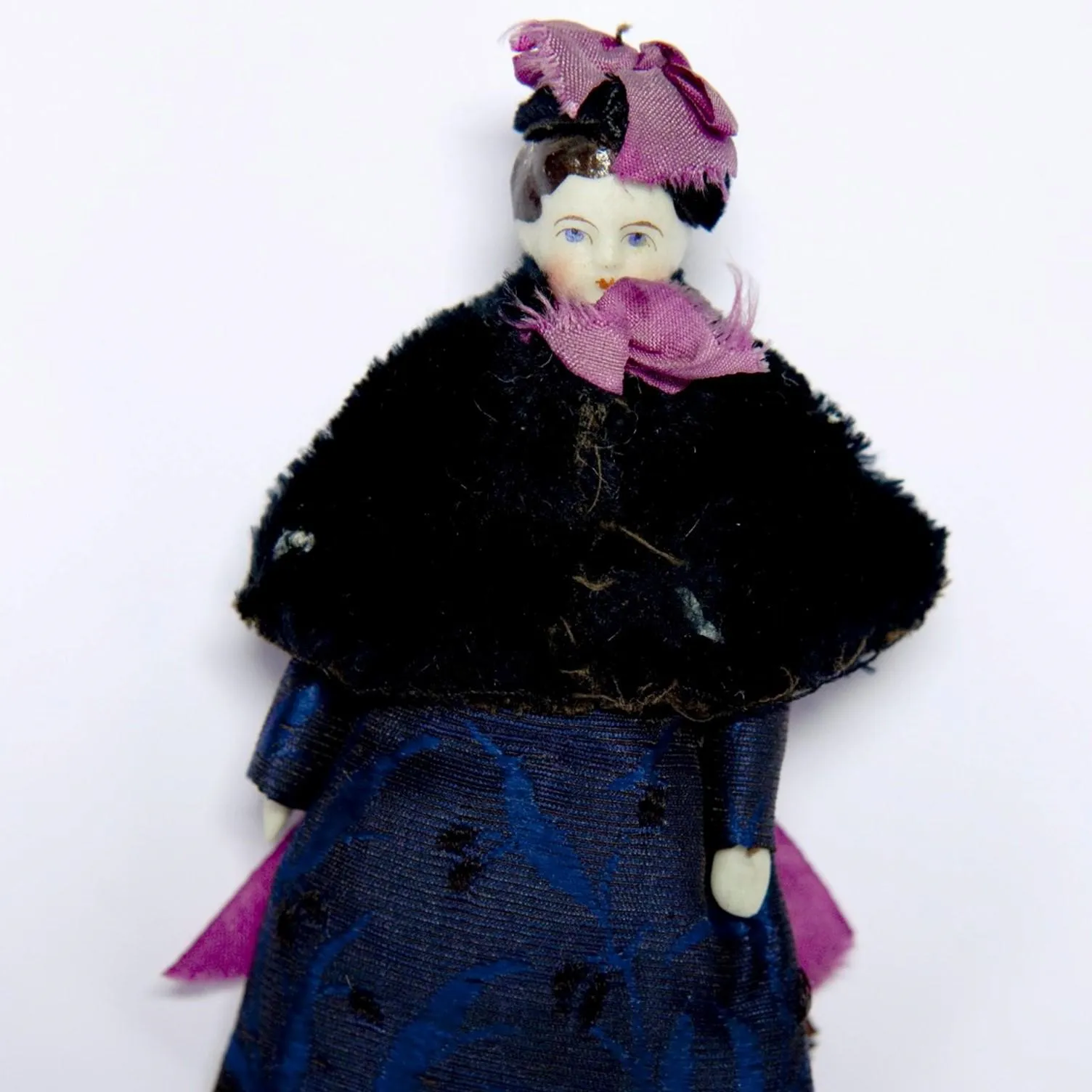 Victorian china doll of a young girl in a black cape and purple ribbons