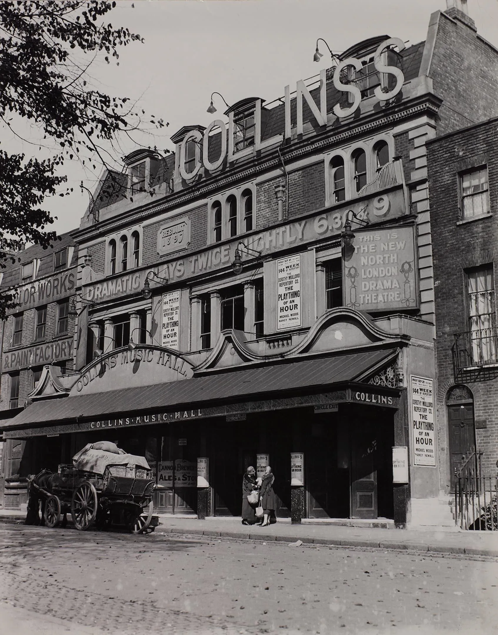 front of collins music hall building with bold signs and a cart parked outside and two people chat.