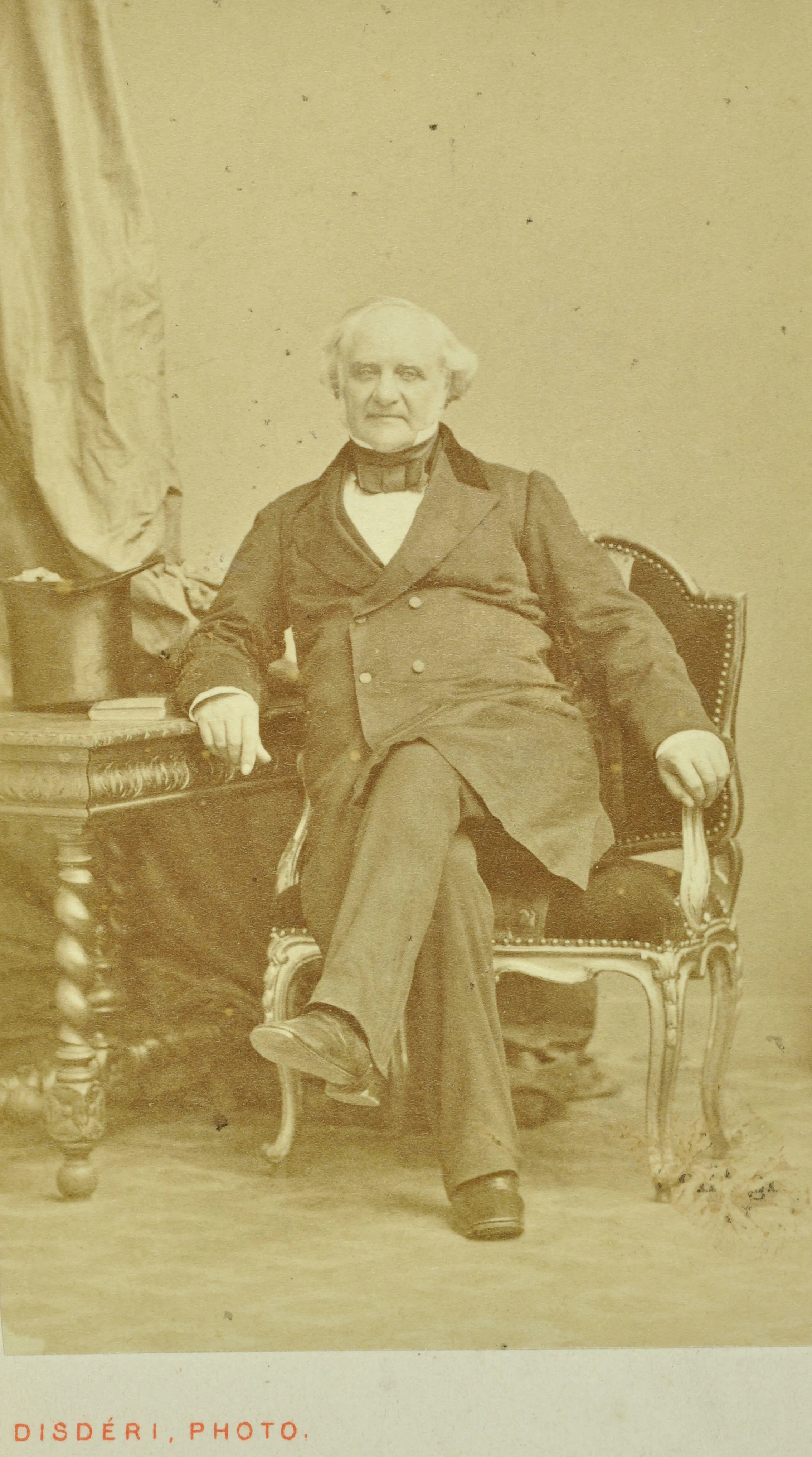 a photograph of George Peabody sitting in a chair with his arm resting on a table next to a top hat