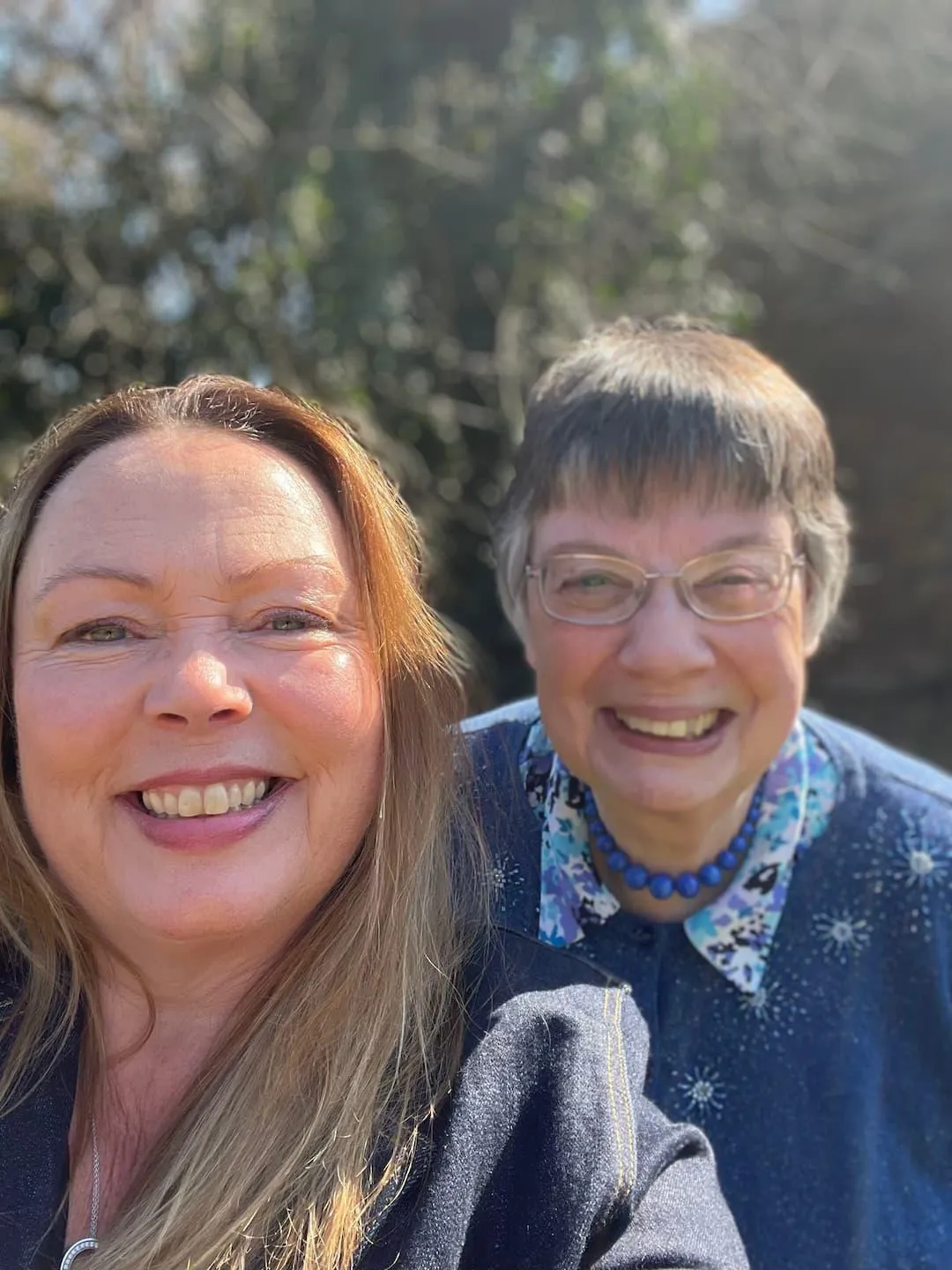 two women taking a selfie, one older woman with glasses behind a younger woman with long hair