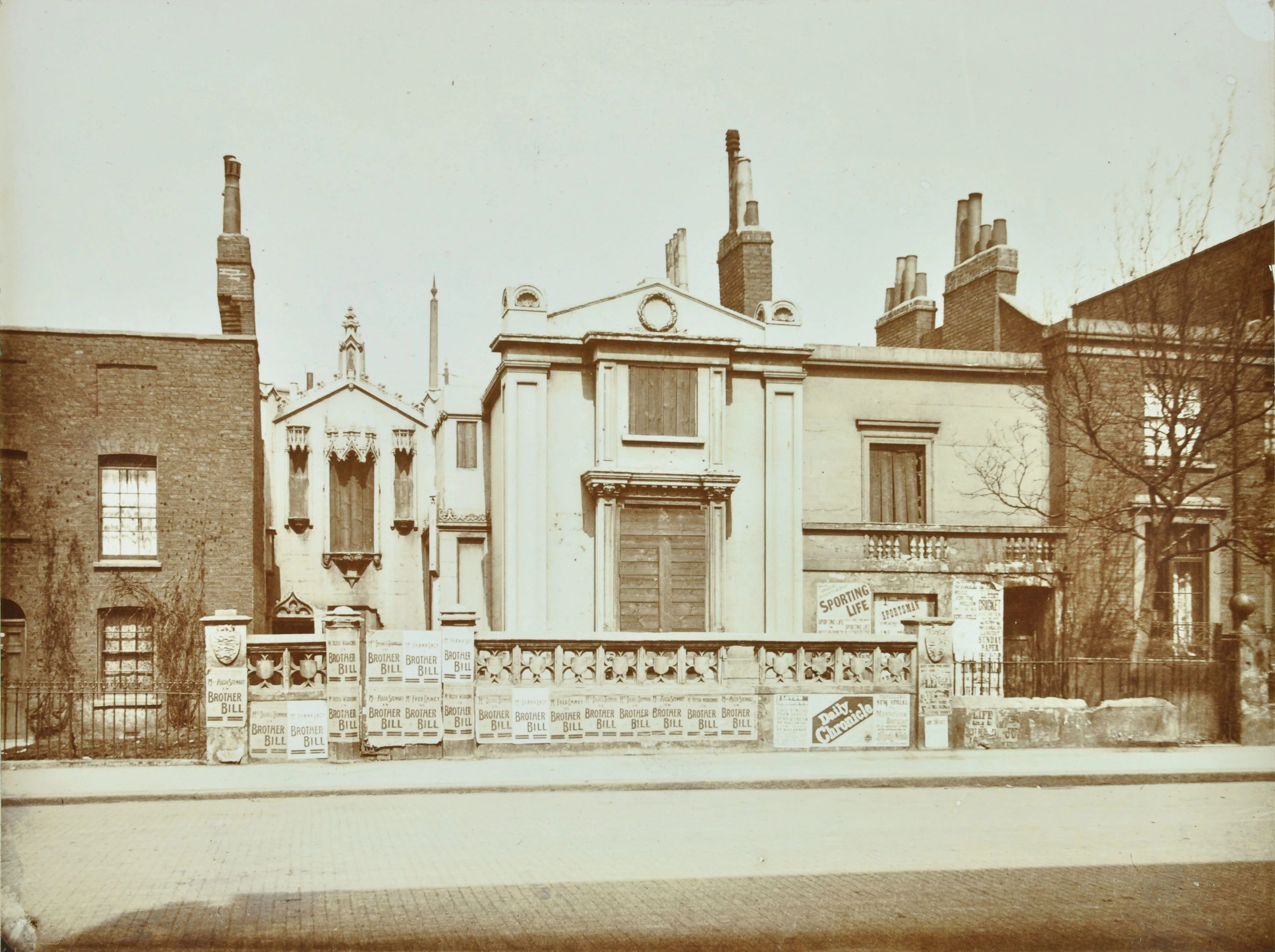 photograph of a variety of houses with playbills pasted on the stone wall.