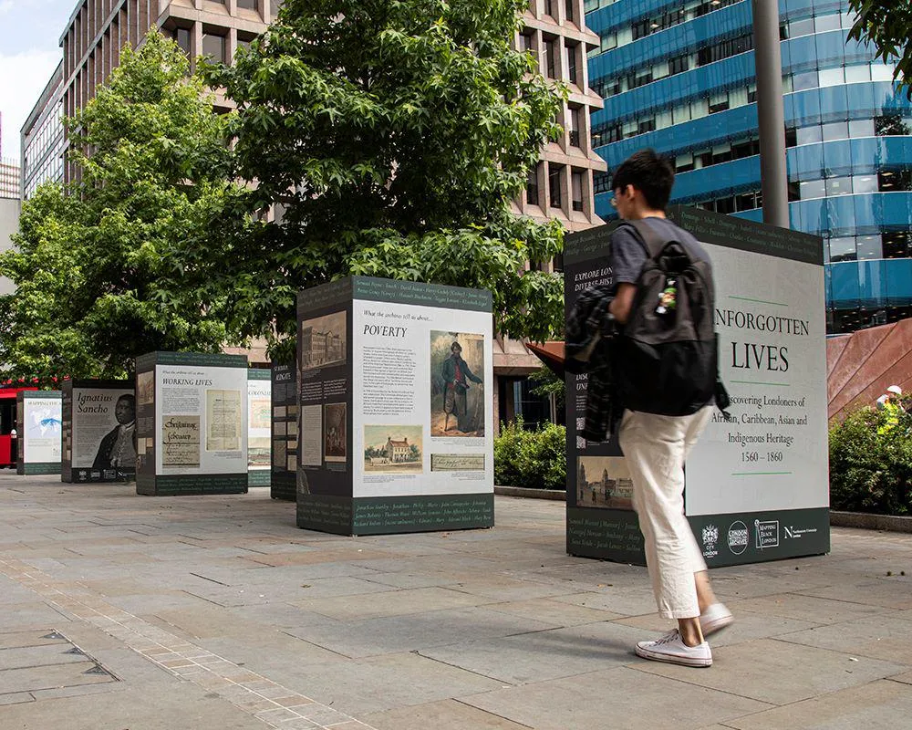 Person walking past exhibition display stands in Aldgate Square