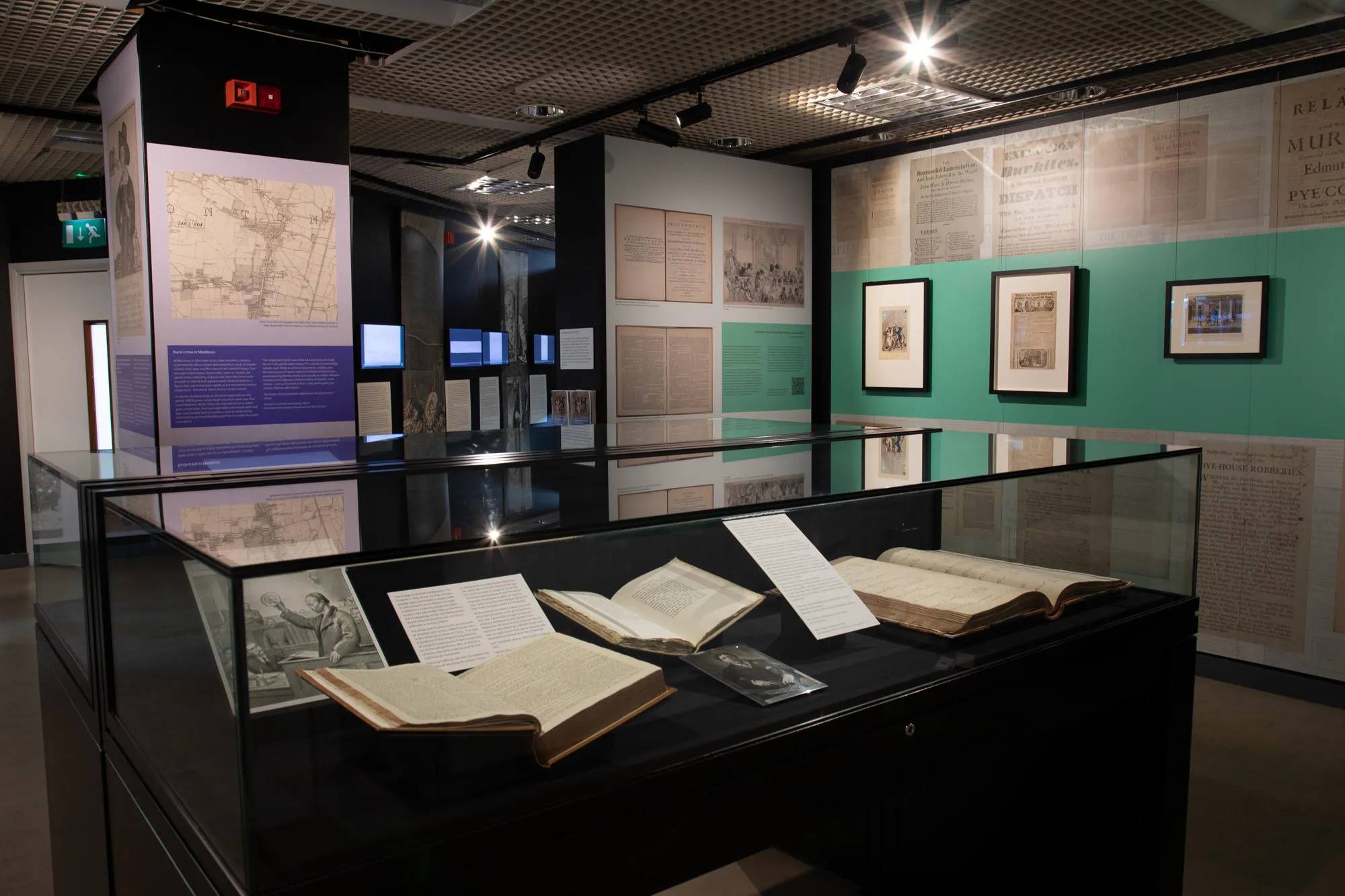 a glass exhibition case is in a small room with documents in the case and on the walls