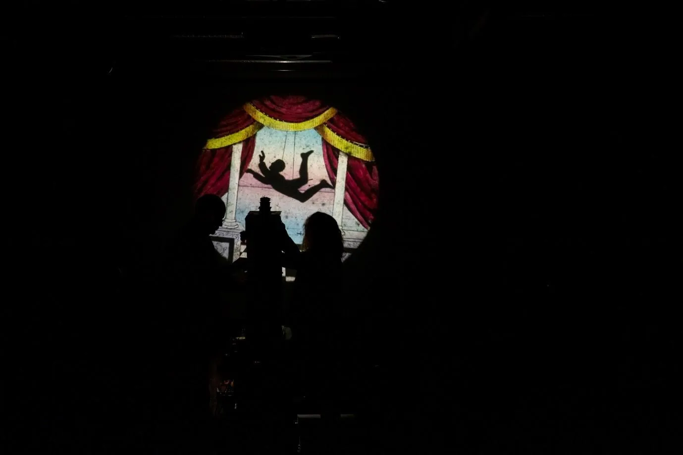 an acrobat flies through the air with red theatre curtains either side