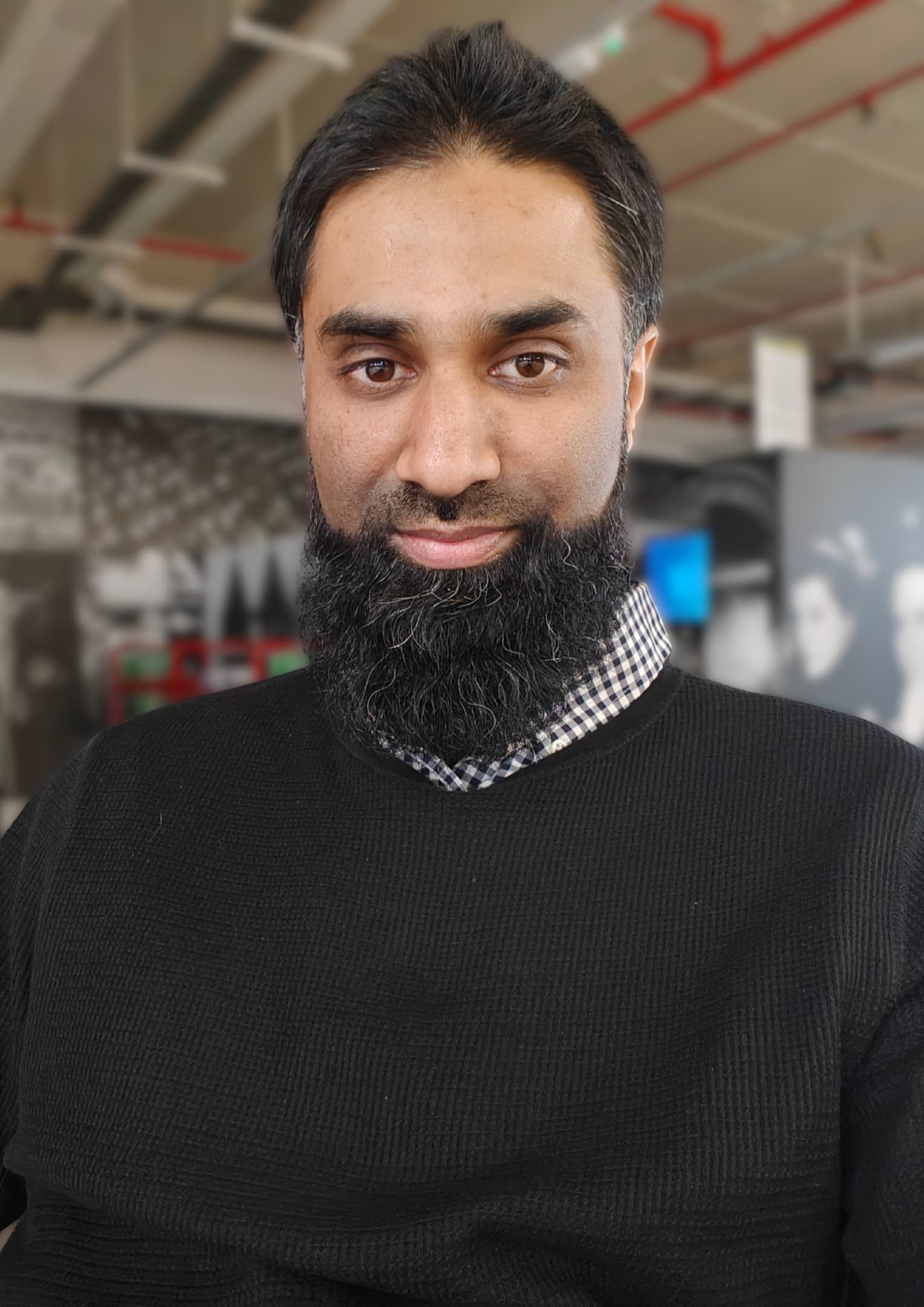 Portrait of Zeshan Ullah Qureshi - man with a beard, shirt and black jumper