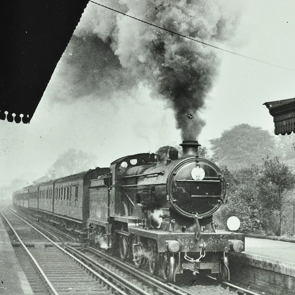 Steam train pulling in to a station, with lots of smoke billowing from the engine