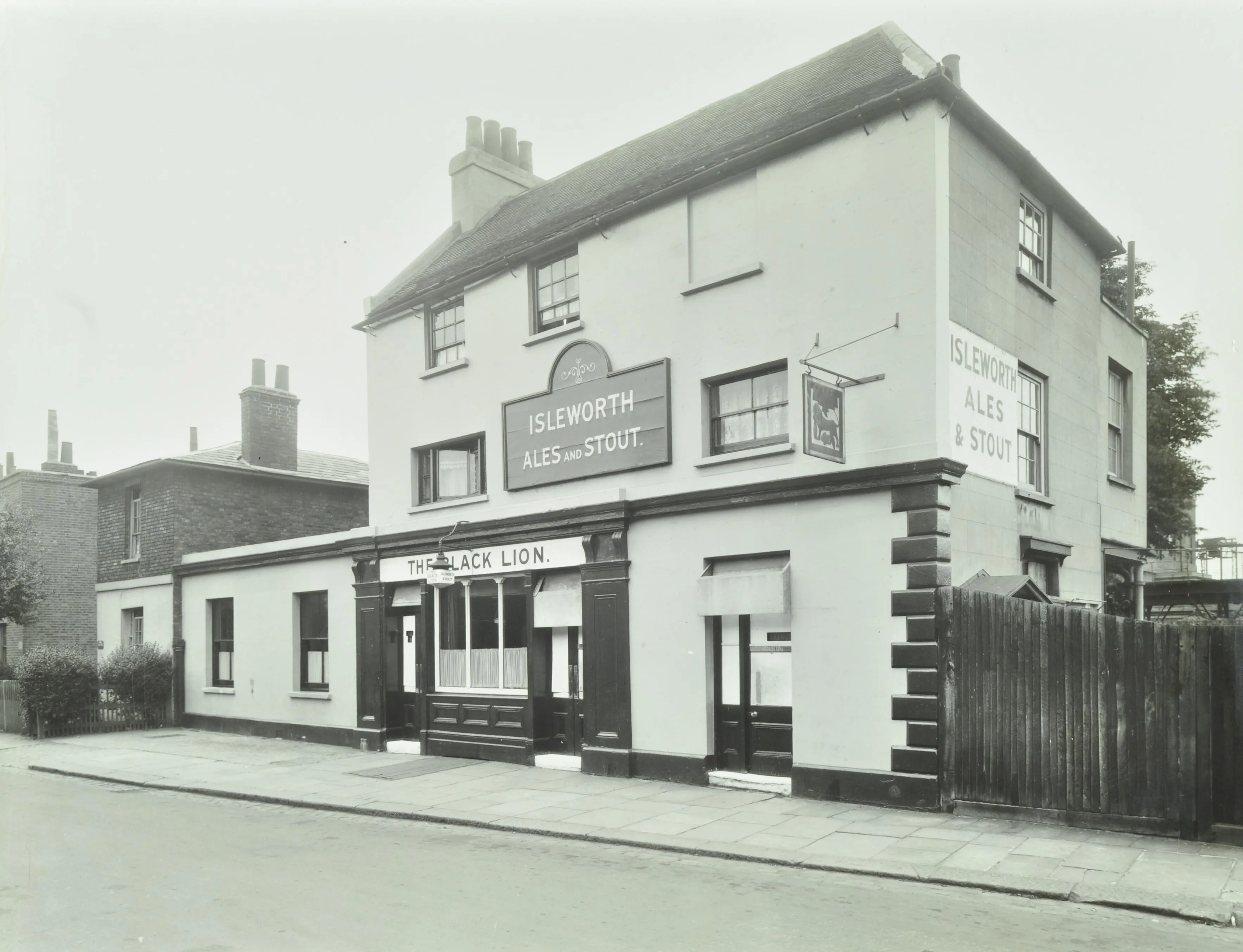 Outside of a pub, black doors, white sign that reads "The Black Lion", and another that reads "Isleworth Ales and Stout".