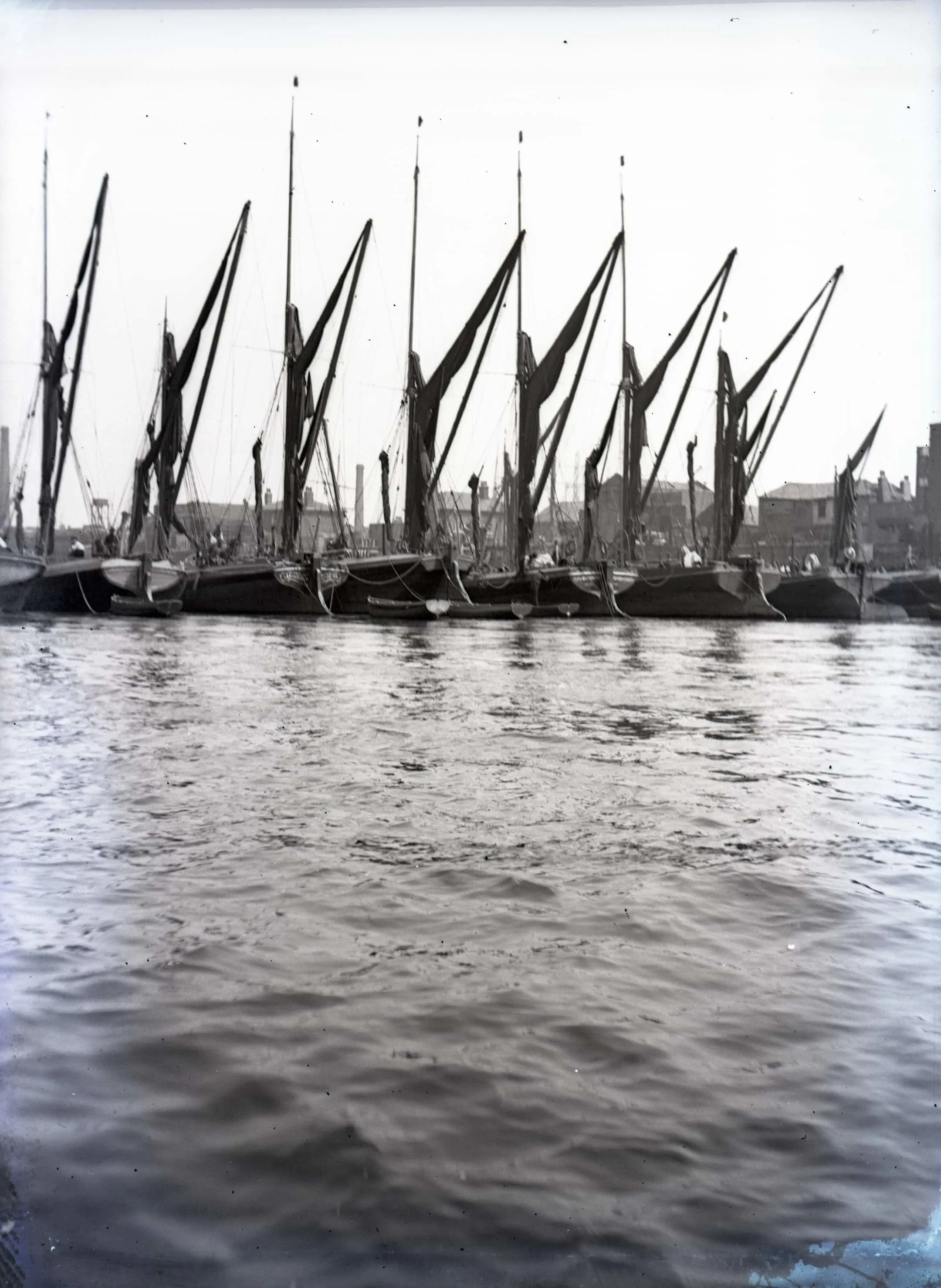 barges with large sails in a line on the river