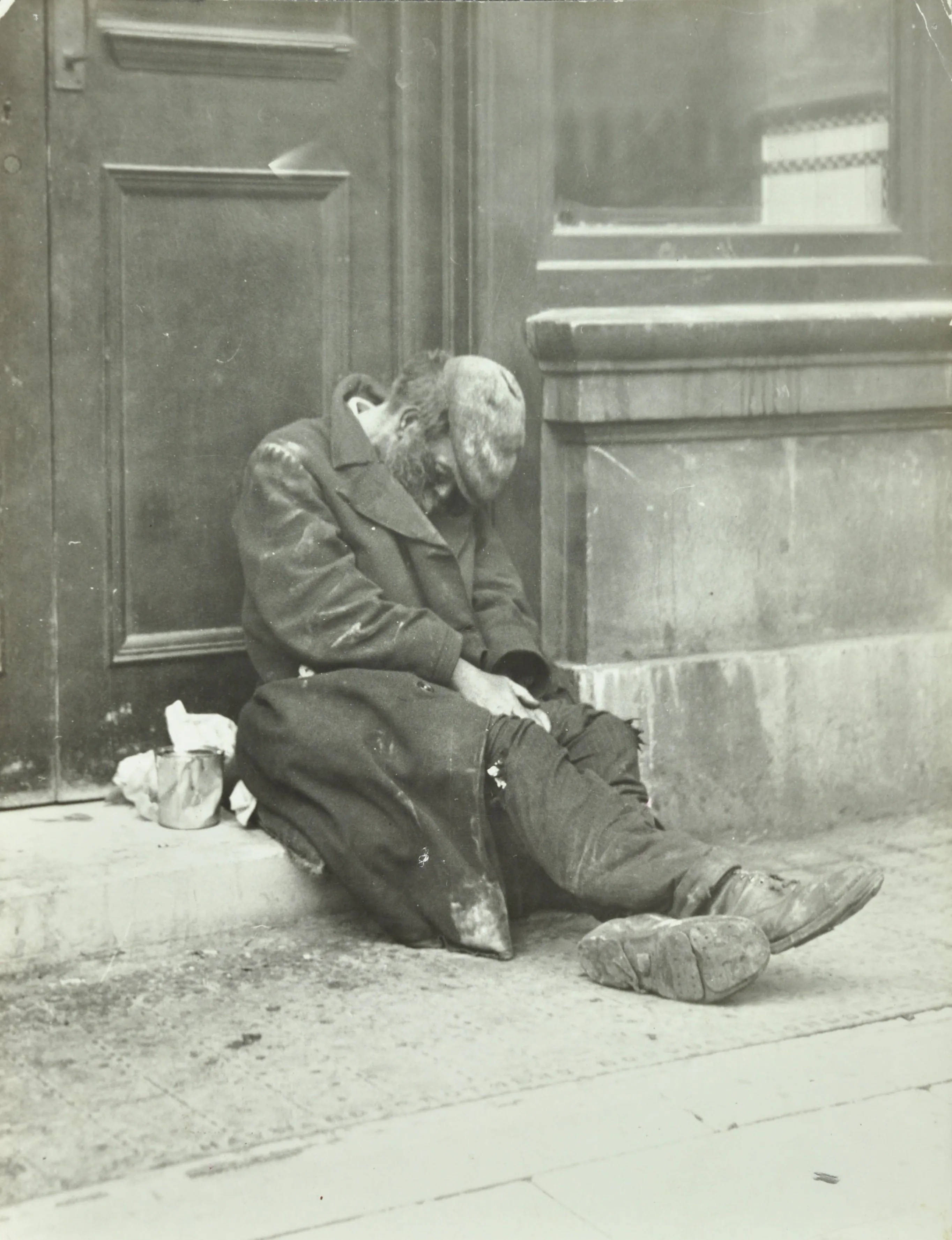 A tramp figure on a doorstep with head in coat