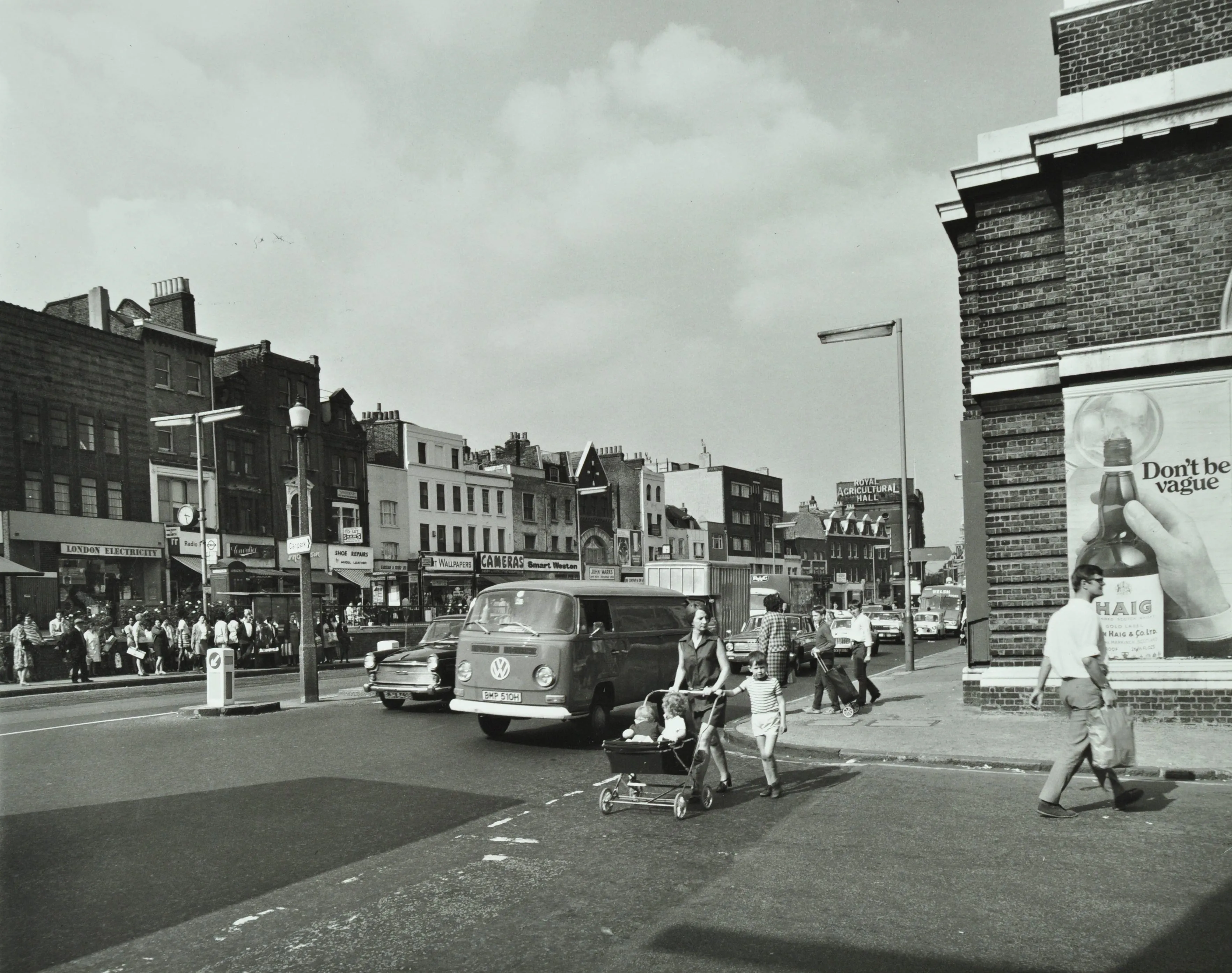 a woman crosses a road with a pushchair as a camper van passes by on a busy shopping street
