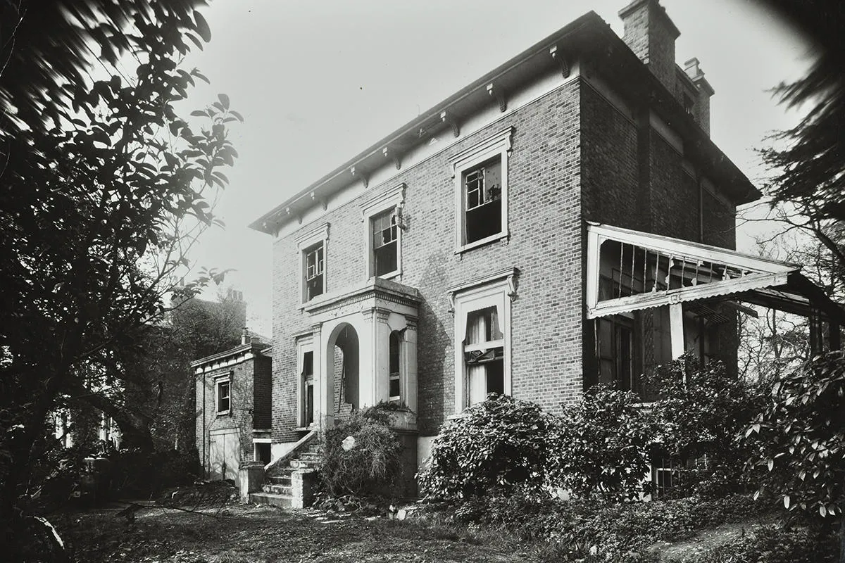 A large house with broken windows and bushes in the foreground